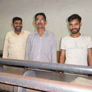 Three men standing in front of a box making machine.